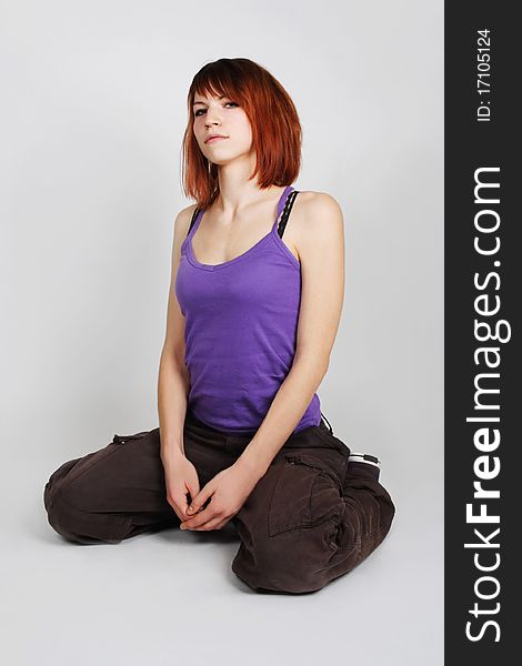 Young redhead girl in hip-hop clothes sitting and looking at camera, full body