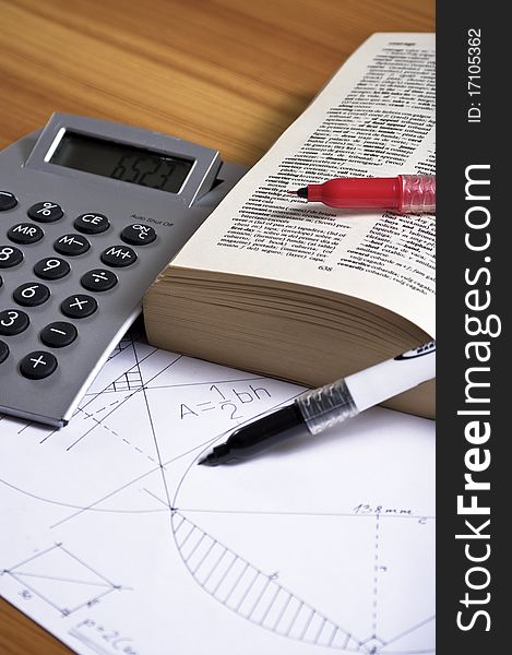 Geometry paper with book, markers and calculator on wooden desk. Geometry paper with book, markers and calculator on wooden desk.