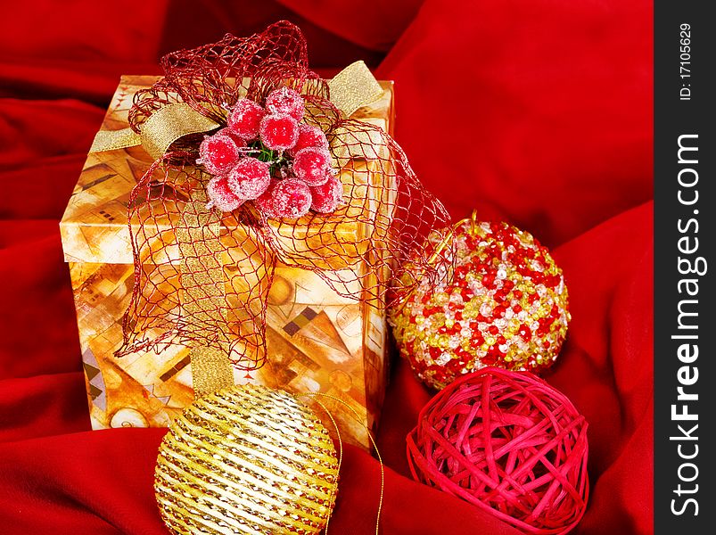 Present box and three Christmas balls over red silk