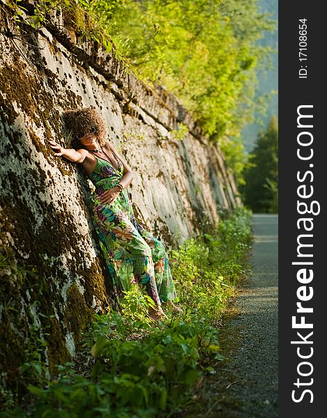 Beatiful girl near wall against the backdrop of lush nature