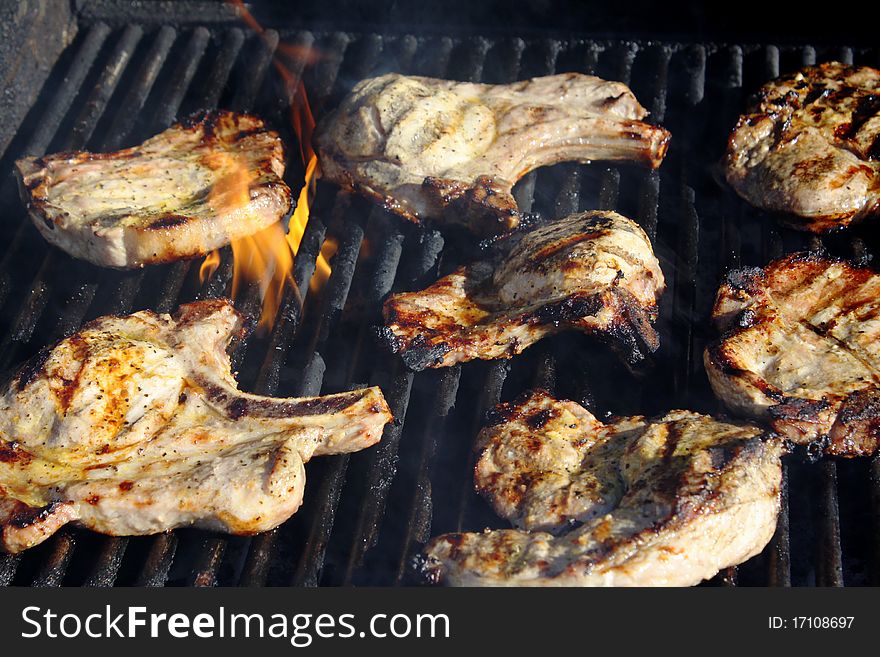 Pork chops being cooked outdoors on a gass grill.