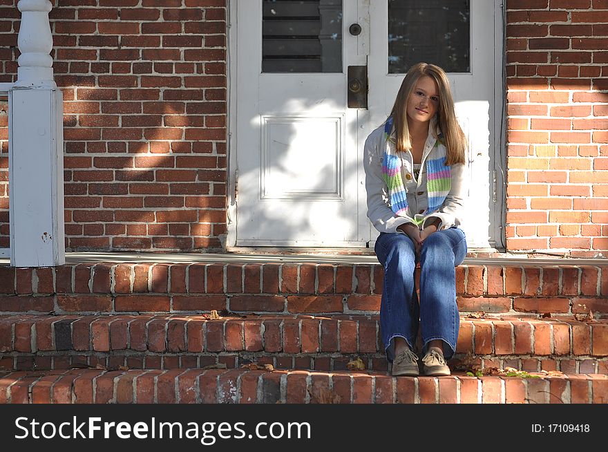 Pretty teen girl with long blonde hair wearing blue jeans sits on the front steps. Pretty teen girl with long blonde hair wearing blue jeans sits on the front steps.
