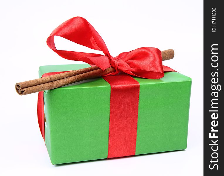 Gift in green wrapping with a red bow decorated with cinnamon stick on white background. Gift in green wrapping with a red bow decorated with cinnamon stick on white background