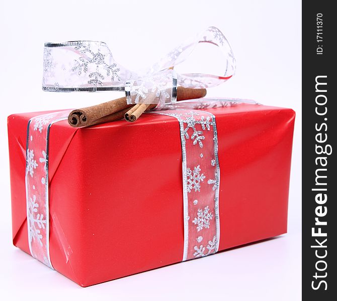 Gift in red wrapping with a silver bow decorated with cinnamon sticks on white background. Gift in red wrapping with a silver bow decorated with cinnamon sticks on white background