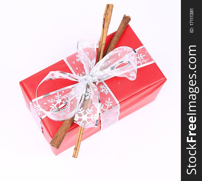 Gift in red wrapping with a silver bow decorated with cinnamon sticks on white background. Gift in red wrapping with a silver bow decorated with cinnamon sticks on white background