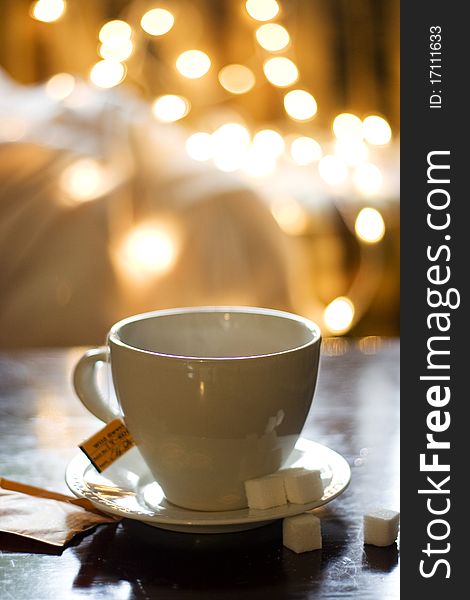 A white tea cup with sugar cubes and an orange tea packet on the side. Bokeh in background. A white tea cup with sugar cubes and an orange tea packet on the side. Bokeh in background.