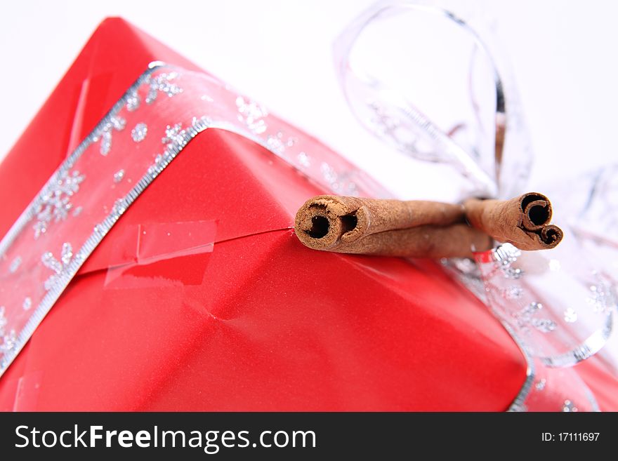 Gift in red wrapping with a silver bow decorated with cinnamon sticks in close up. Gift in red wrapping with a silver bow decorated with cinnamon sticks in close up