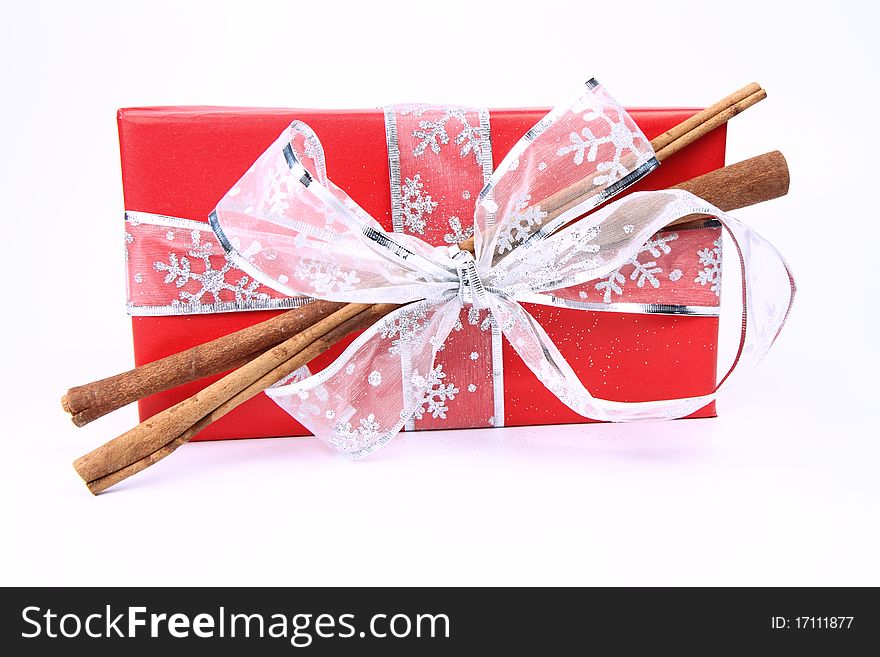 Gift in red wrapping with a silver bow decorated with cinnamon sticks on white background. Gift in red wrapping with a silver bow decorated with cinnamon sticks on white background