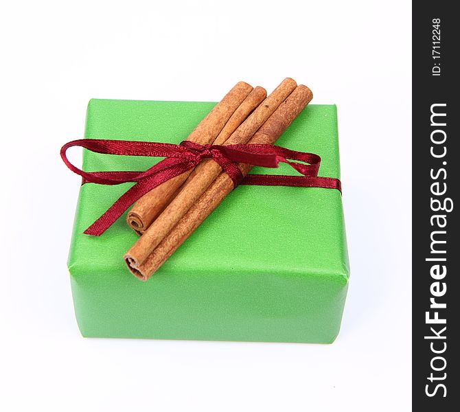Gift in green wrapping with a red bow decorated with cinnamon sticks on white background. Gift in green wrapping with a red bow decorated with cinnamon sticks on white background
