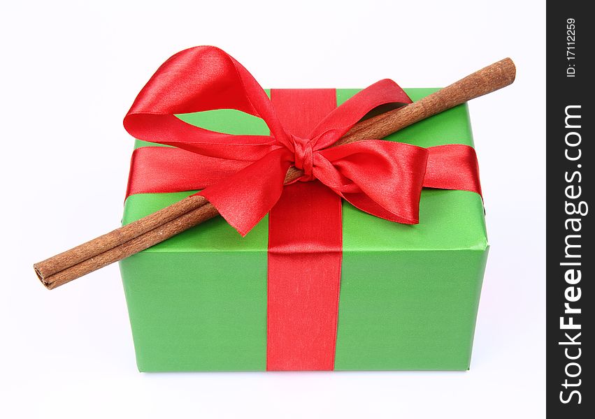Gift in green wrapping with a red bow decorated with cinnamon stick on white background. Gift in green wrapping with a red bow decorated with cinnamon stick on white background