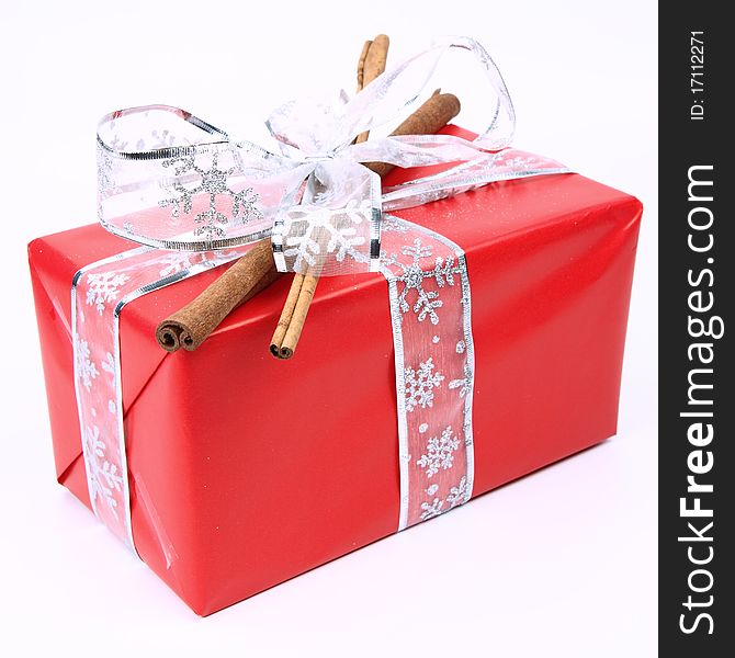 Gift in red wrapping with a silver bow decorated with cinnamon sticks on white background. Gift in red wrapping with a silver bow decorated with cinnamon sticks on white background