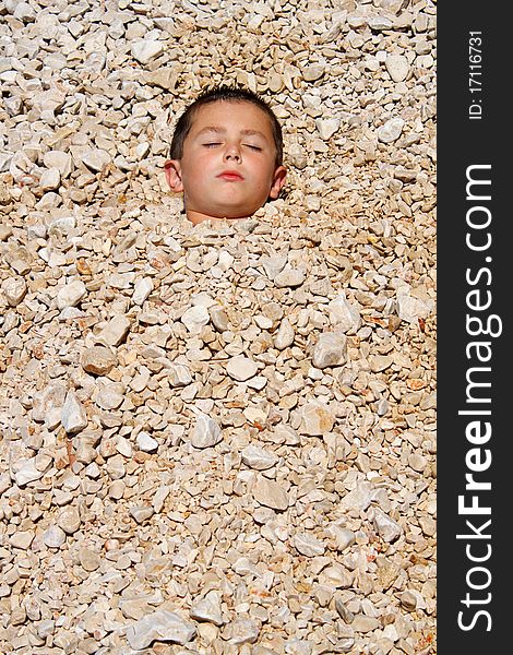 Boy buried in the pebbles on the beach