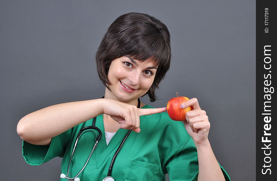 Attractive lady doctor pointing to a fresh apple on gray background