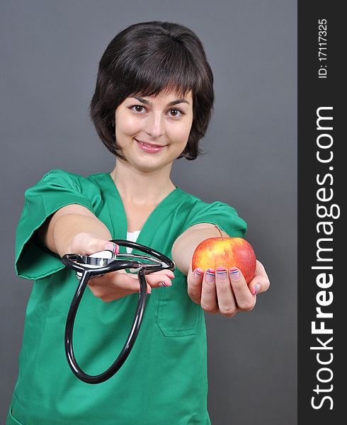 Attractive lady doctor with stethoscope and fresh apple on gray background