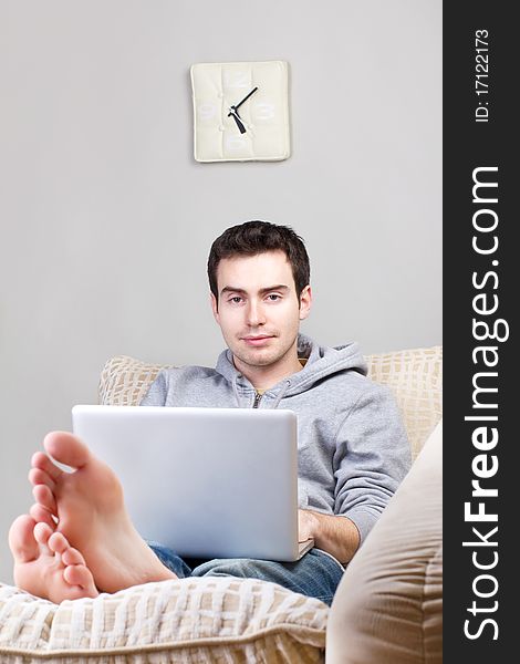 Smiling young man using laptop and lying on the sofa at home. Smiling young man using laptop and lying on the sofa at home