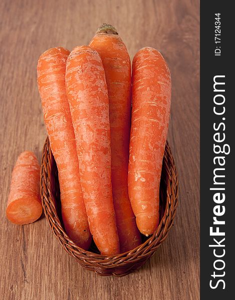 Fresh carrots in a wicker basket on an old wooden table