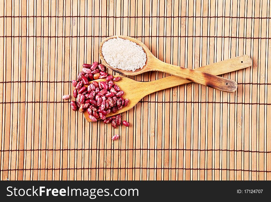 Wooden spoons with beans and rice over bamboo sticks background