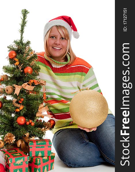 Young woman with santa hat sitting beside a christmas tree with christmas gifts - isolated. Young woman with santa hat sitting beside a christmas tree with christmas gifts - isolated