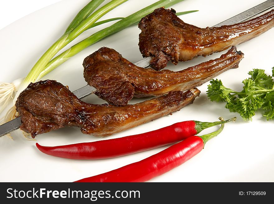 Grilled meat on the bone and on skewer with fresh vegetables: parsley, paprika and onion on a white plate. Grilled meat on the bone and on skewer with fresh vegetables: parsley, paprika and onion on a white plate