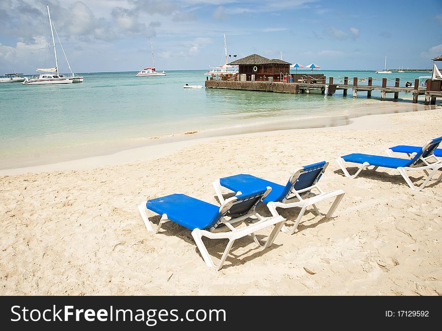 Empty blue beach chairs on a sandy beach overlooking the Caribbean Sea on a sunny day. Empty blue beach chairs on a sandy beach overlooking the Caribbean Sea on a sunny day.