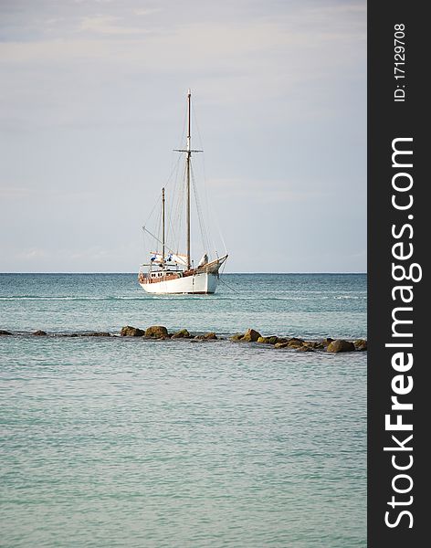 A sailboat anchored off shore in the Caribbean with rocks in the foreground.
