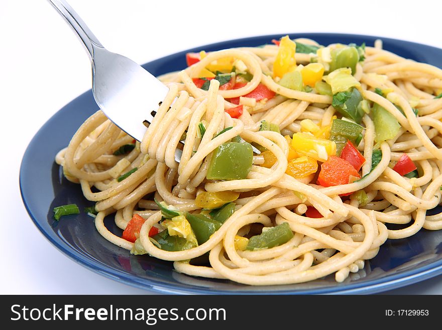 Spaghetti with vegetables being eaten with a fork on white background