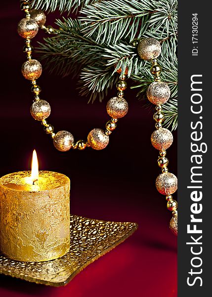 On a red background, a burning candle, fir branch and a ball chain. On a red background, a burning candle, fir branch and a ball chain.