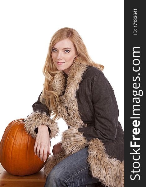 A woman sitting in her warm fuzzy coat while she leans on a pumpkin. A woman sitting in her warm fuzzy coat while she leans on a pumpkin.