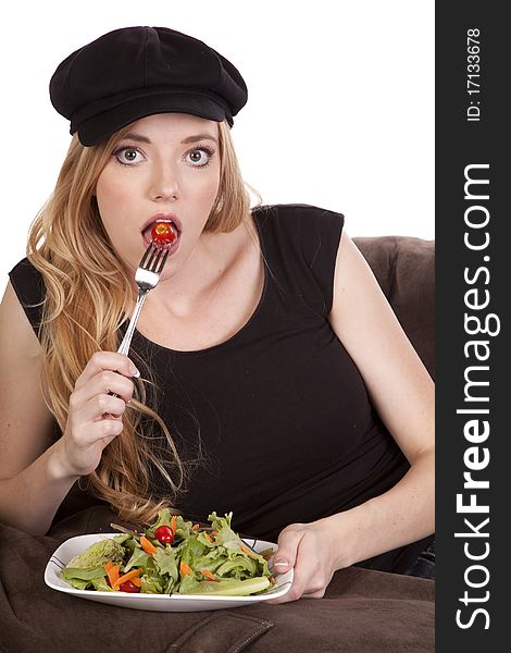A woman sitting on a bean bag getting ready to eat a tomato while she is enjoying her nice green salad. A woman sitting on a bean bag getting ready to eat a tomato while she is enjoying her nice green salad.