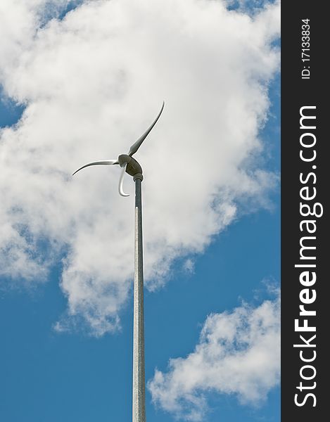 A spinning windmill with curved blades turns in front of a blue sky and white clouds. A spinning windmill with curved blades turns in front of a blue sky and white clouds.