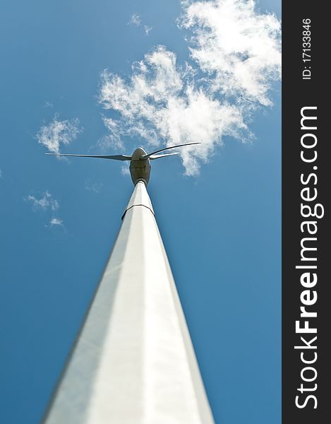 A spinning windmill with curved blades turns in front of a blue sky and white clouds. Low angle shot. A spinning windmill with curved blades turns in front of a blue sky and white clouds. Low angle shot.