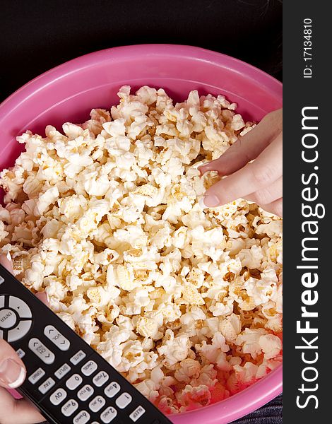 A close up of a remote for the tv and a persons hand reaching for some popcorn. A close up of a remote for the tv and a persons hand reaching for some popcorn.