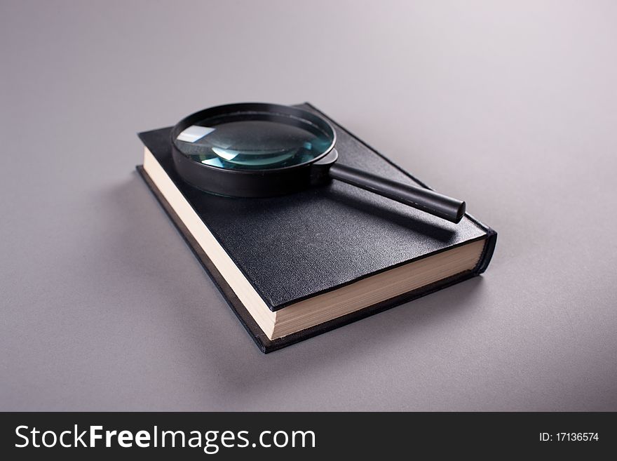 Magnifying glass on closed book on grey