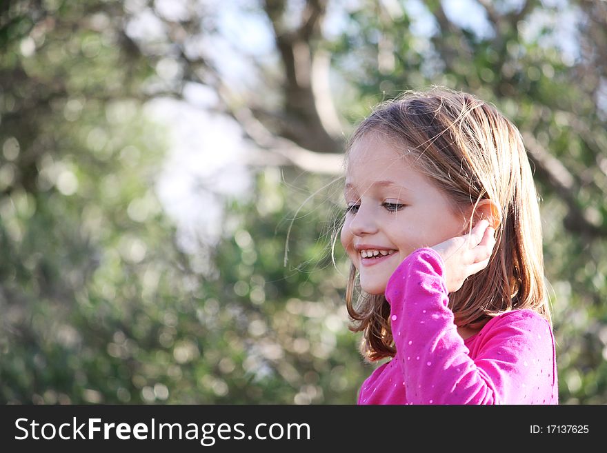 Profile portrait of a happy female child smiling outdoors with natural bokeh background