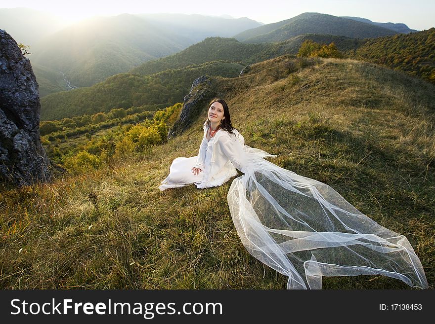 Romantic woman with long veil sitting on hill. Romantic woman with long veil sitting on hill
