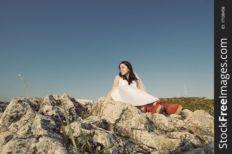 Romantic woman with red boots sitting on rocks