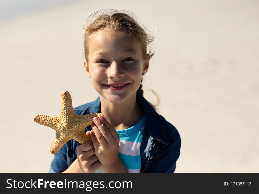 Portrait close up of a Caucasian girl on a sunny beach, holding up a starfish in her hand, looking to camera and smiling. Portrait close up of a Caucasian girl on a sunny beach, holding up a starfish in her hand, looking to camera and smiling