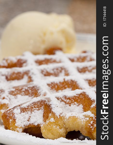 A close-up a waffle on a white plate sprinkled with sugar over and ice-cream. A close-up a waffle on a white plate sprinkled with sugar over and ice-cream