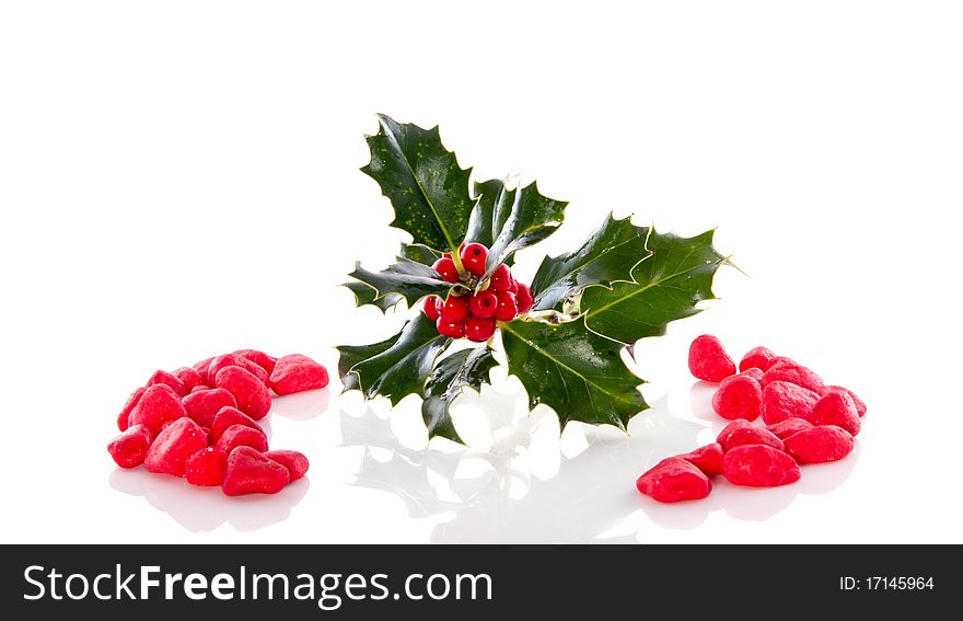 A christmas holly branch between decorative stones isolated over white