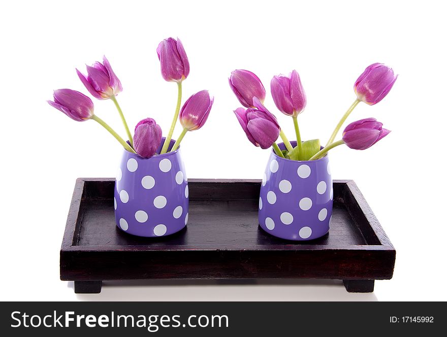 Two little vases with purple tulips on a wooden tray isolated over white