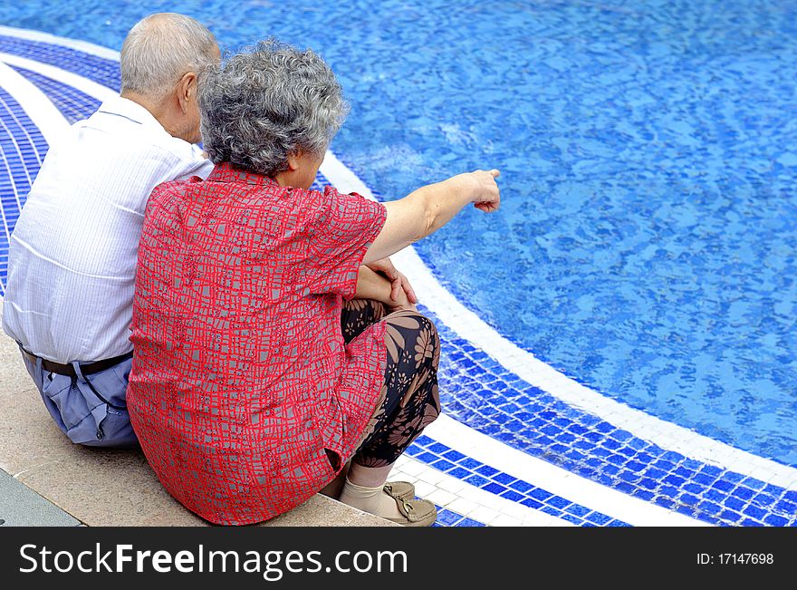 An intimate senior couple sitting beside a pool. An intimate senior couple sitting beside a pool