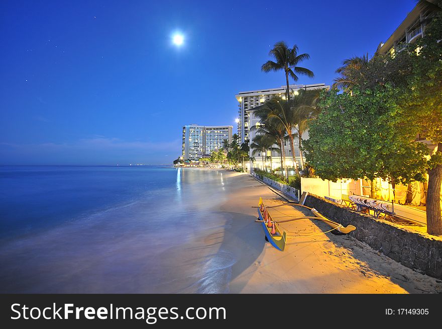 An outrigger in the sandy beach with full moon and hotels. An outrigger in the sandy beach with full moon and hotels
