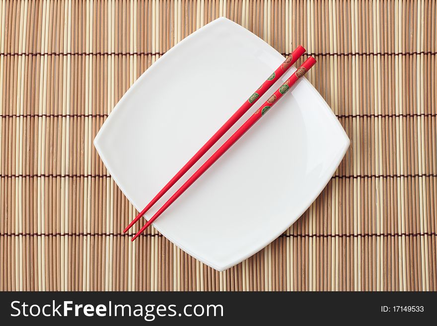 Red chopsticks and white dish on a bamboo napkin. Close-up