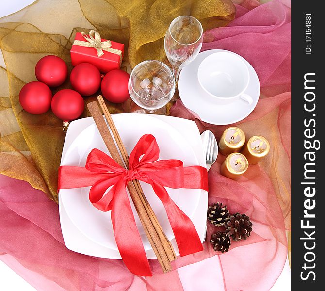 Christmas setting-a plate decorated with cinnamon sticks and ribbon, a cup, glasses, christmas balls, candles, gift and cones