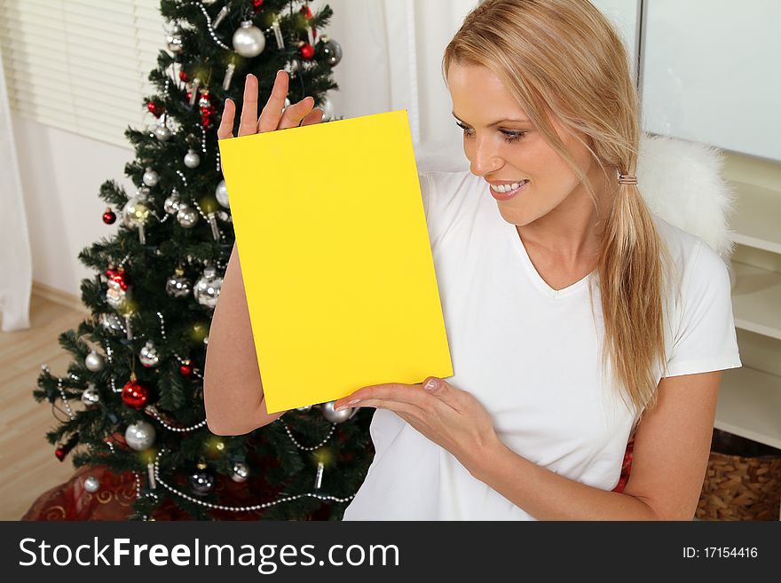 blond angel standing in front of a christmas tree holding a sign. blond angel standing in front of a christmas tree holding a sign