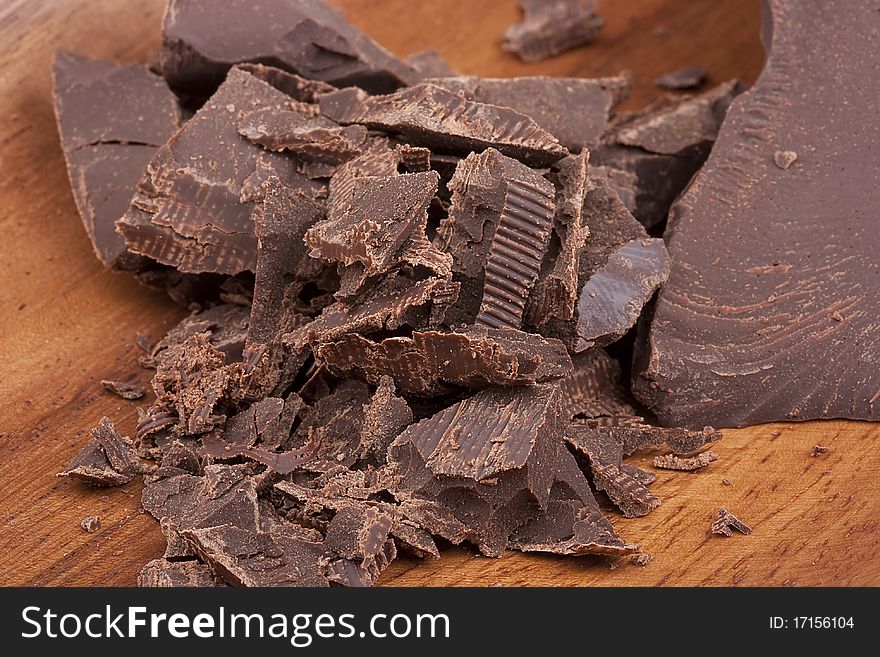 Bitter chocolate in pieces on a brown background in a plate.