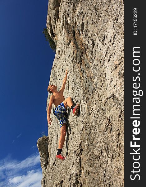 A guy climbs on a rock against the blue sky. A guy climbs on a rock against the blue sky