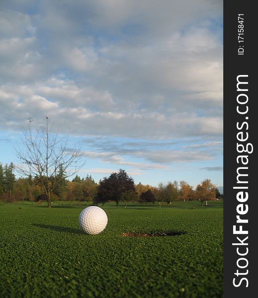 Photo of golf ball on the green beside the hole.