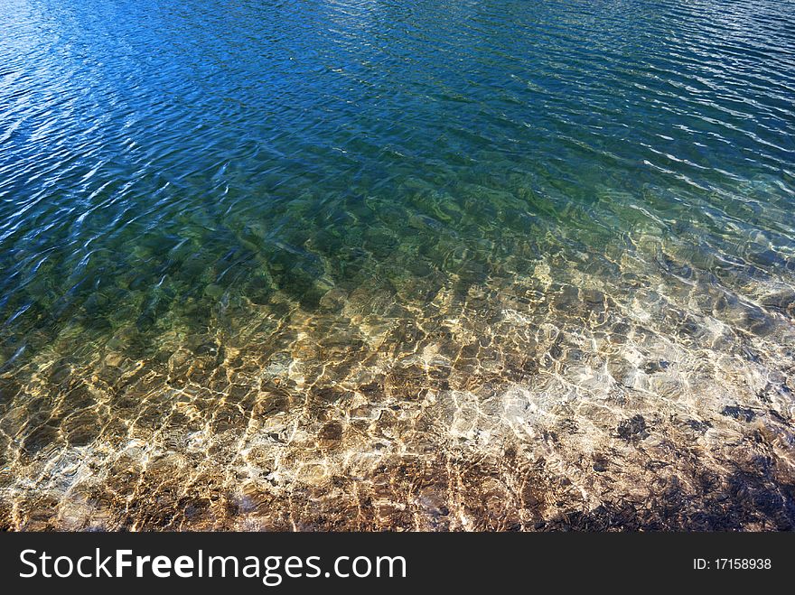 Looking into the water of a clear mountain lake with the blue sky reflected off the ripples in the water. Looking into the water of a clear mountain lake with the blue sky reflected off the ripples in the water.