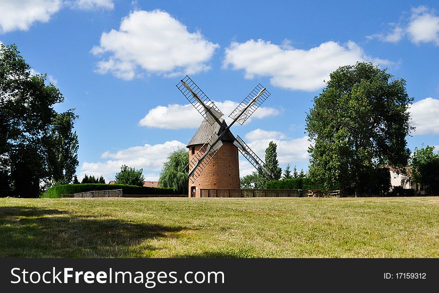 Reovanted windmill in a field with blue sky and clouds background. Reovanted windmill in a field with blue sky and clouds background